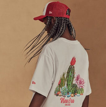 girl wearing a red mesh cap & a white graphic tee of a cactus with flowers