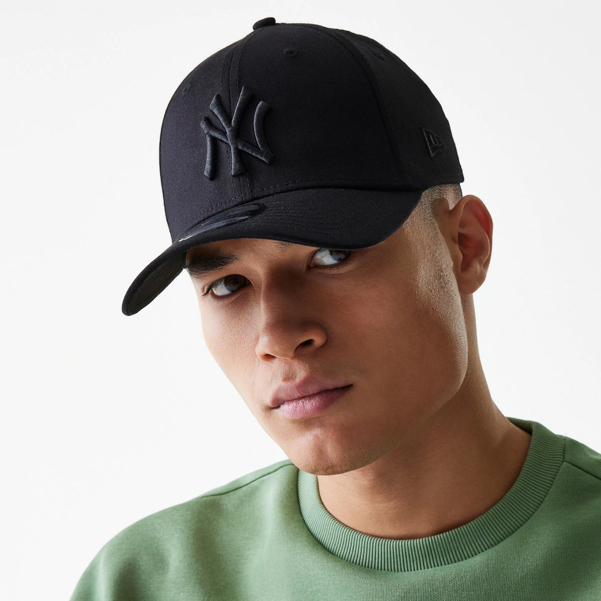 New York Yankees Classic Black New Era 39THIRTY Cap, on-model front view with raised embroidered NY logo on the structured crown, black curved visor, and New Era flag logo on the left side, paired with a green sweatshirt.
