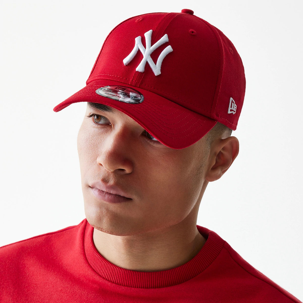 New York Yankees Essential Red New Era 9FORTY Cap, on-model front view showing the raised white NY logo on the front panel, New Era flag logo on the left side, and a 9FORTY size sticker on the red curved visor.