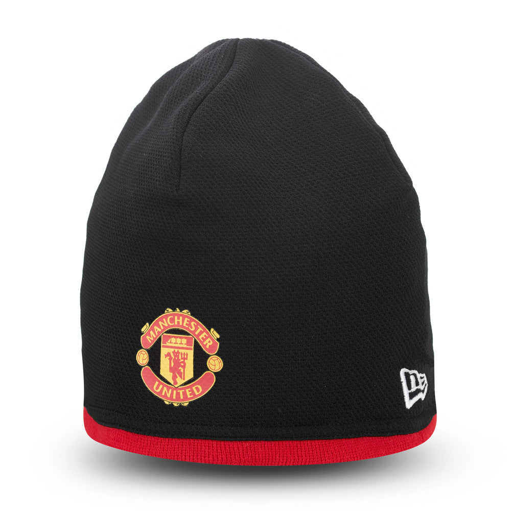 Manchester United Essential Black Beanie Hat, side view with the red and gold club crest on the front, featuring a black knit design and a red band around the base, complemented by the white New Era flag logo on the left side.
