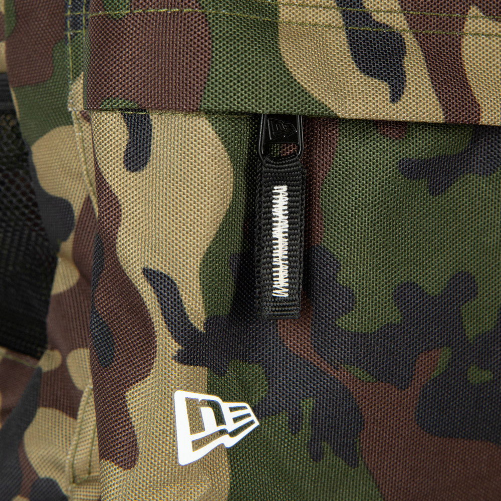 New Era New York Yankees Woodland Camo Stadium Backpack, side view showing the woodland camo pattern with a zip and pull tab at the centre, a raised white New Era logo near the lower corner against the camo background.