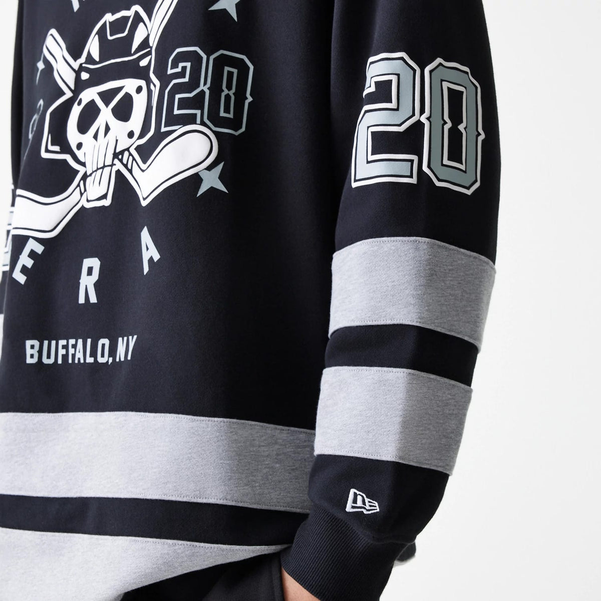 New Era Street Dangle Grey Pullover Hoodie, side view showing the arm with grey and black striped design, a raised New Era logo on the cuff, and a large graphic print of hockey sticks and skull on the chest.