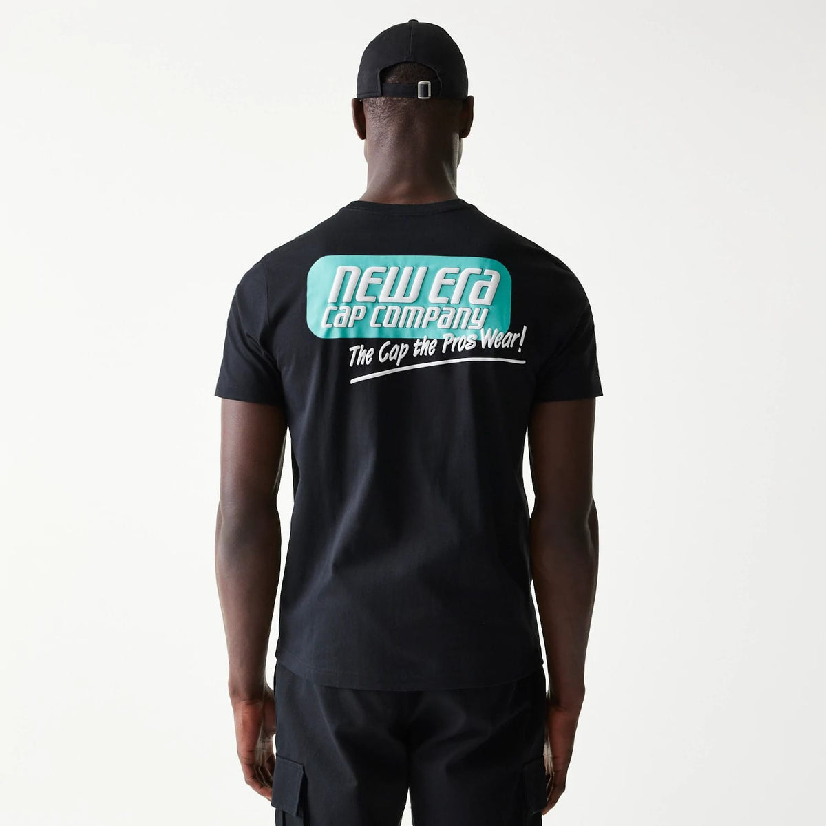 New Era Classic Black T-Shirt, on-model view showing the back with a large printed turquoise and white New Era Cap Company logo and text, paired with a black cap featuring a raised logo on the rear strap.