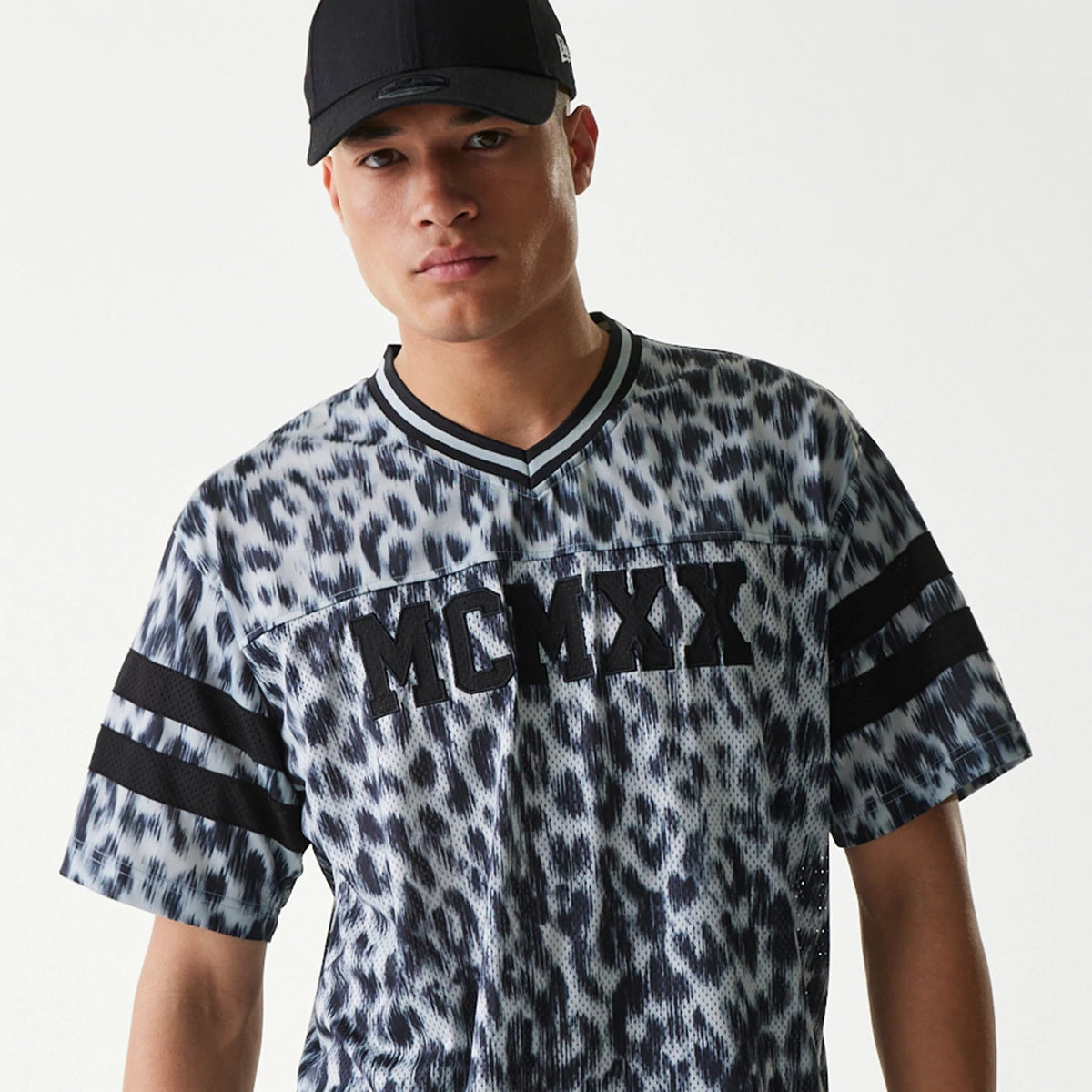 New Era Retro Sports Grey Mesh Jersey, front view on a model wearing a black cap, featuring black MCMXX lettering on the chest, a leopard print pattern, and black horizontal stripes on the sleeves.