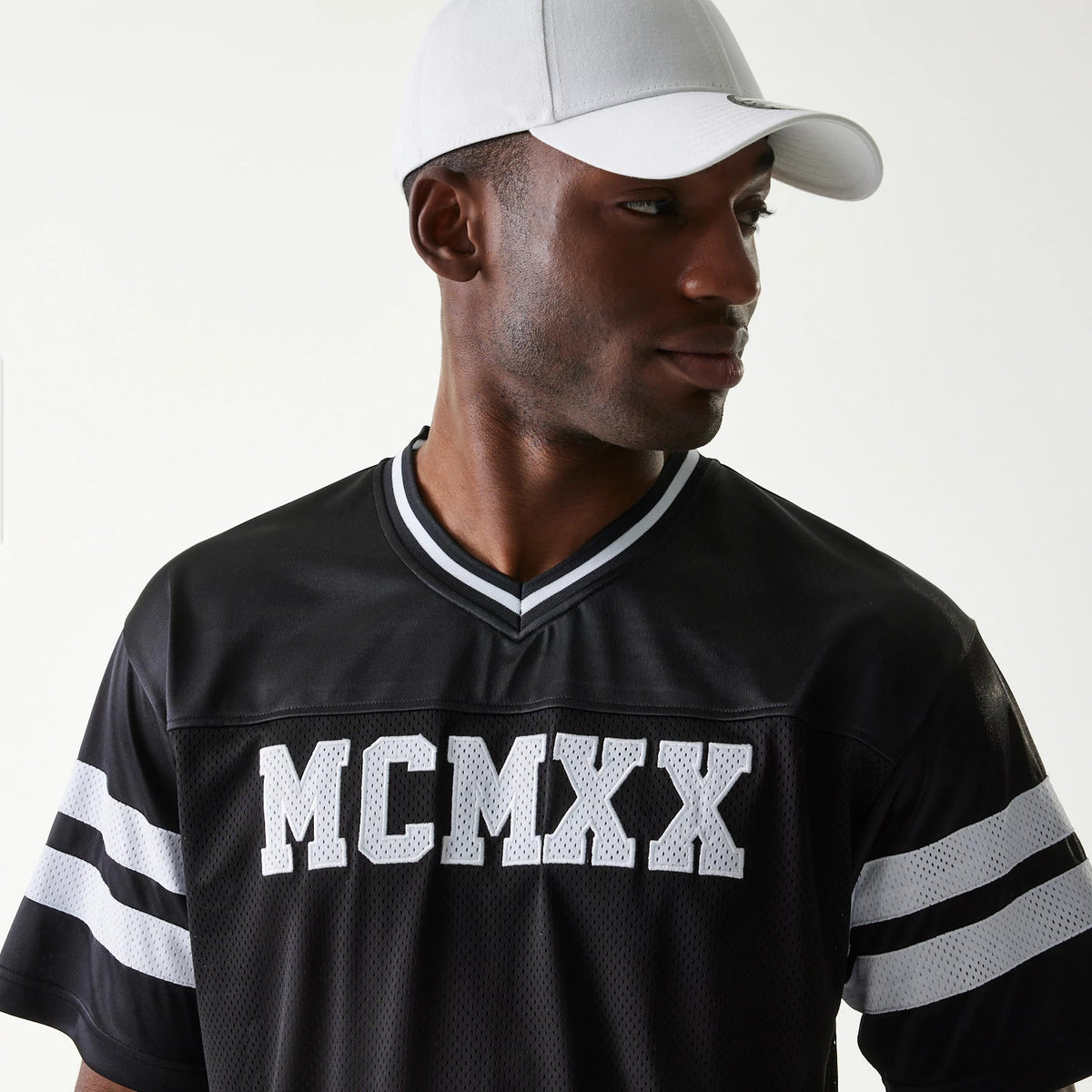 New Era Retro Sports Black Mesh Jersey, front view on a model wearing a white cap, featuring large white MCMXX lettering across the chest and contrasting white stripe details on the sleeves.