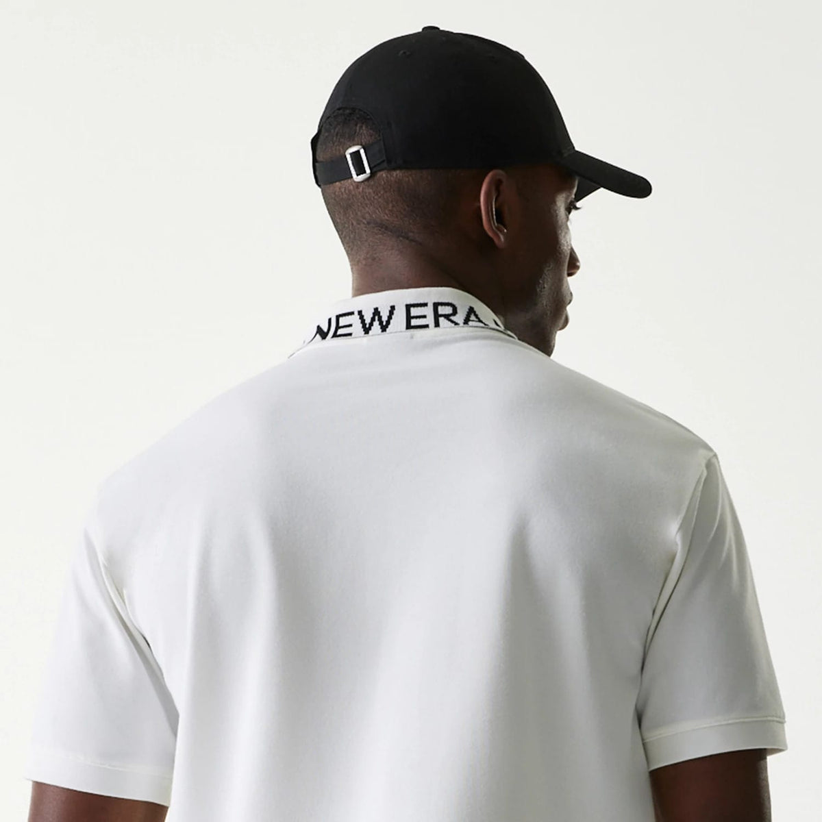 New Era Japan Collar Logo White Polo T-Shirt, rear view showing the black folded collar with New Era text across, short sleeves, and a person wearing a black cap with a debossed logo on the back.