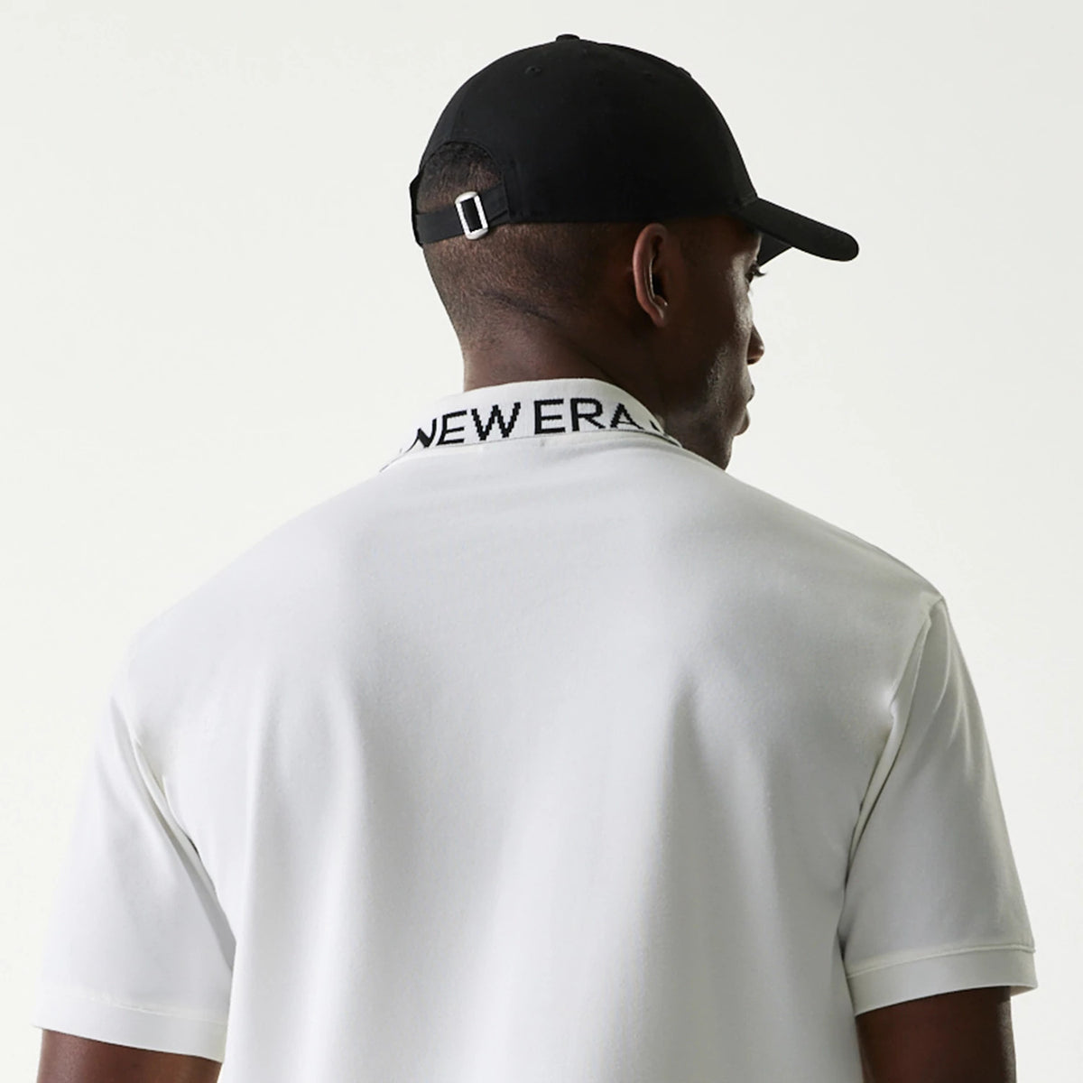 New Era Japan Collar Logo White Polo T-Shirt, rear view showing the black folded collar with New Era text across, short sleeves, and a person wearing a black cap with a debossed logo on the back.