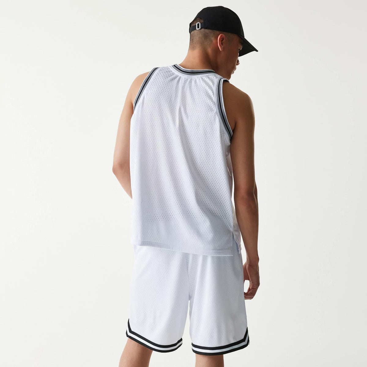 New Era Japan Mesh White Sleeveless T-Shirt, on-model rear view showing the sleeveless white top with dark ribbed trim around the arms and neck, paired with matching shorts, and a black debossed New Era logo on a black cap.