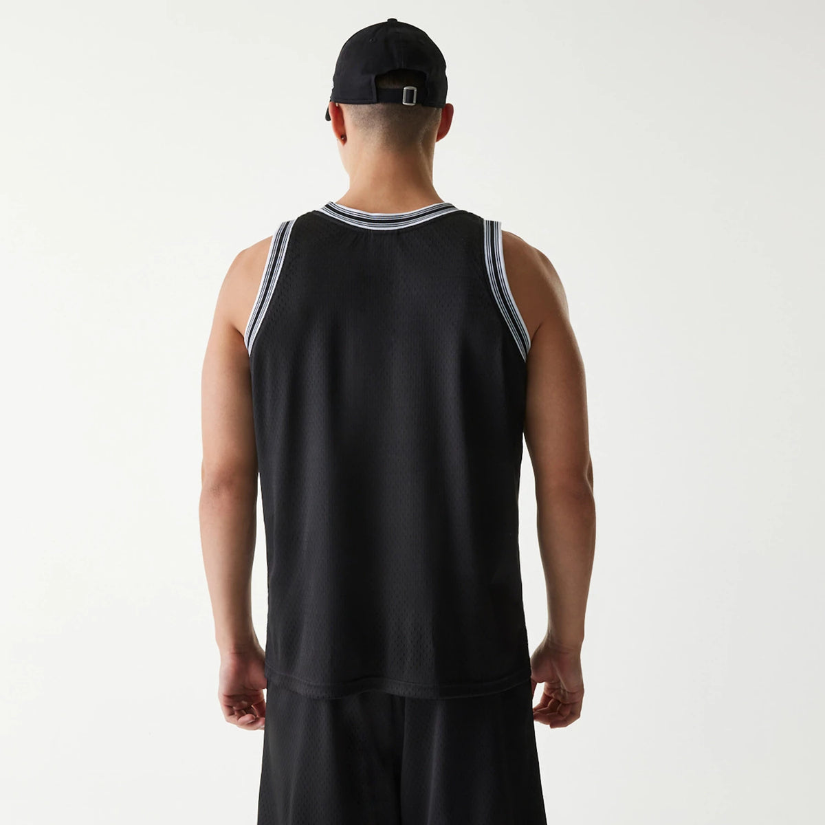 New Era Japan Mesh Black Sleeveless T-Shirt, on-model rear view showing the black mesh fabric with white trim on the shoulders and neck, paired with black shorts and a black cap featuring a debossed logo on the back.