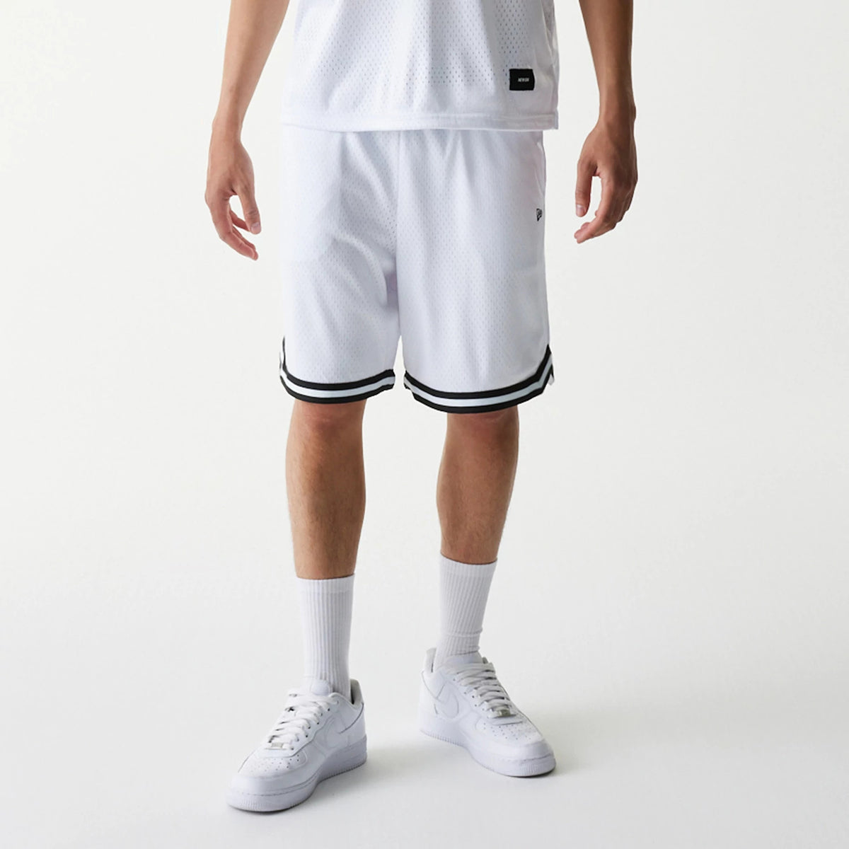New Era Japan Mesh White Shorts, on-model view showing the white mesh fabric with black double stripes at the hem, a small debossed New Era logo on the left leg, and a relaxed fit extending just above the knee.