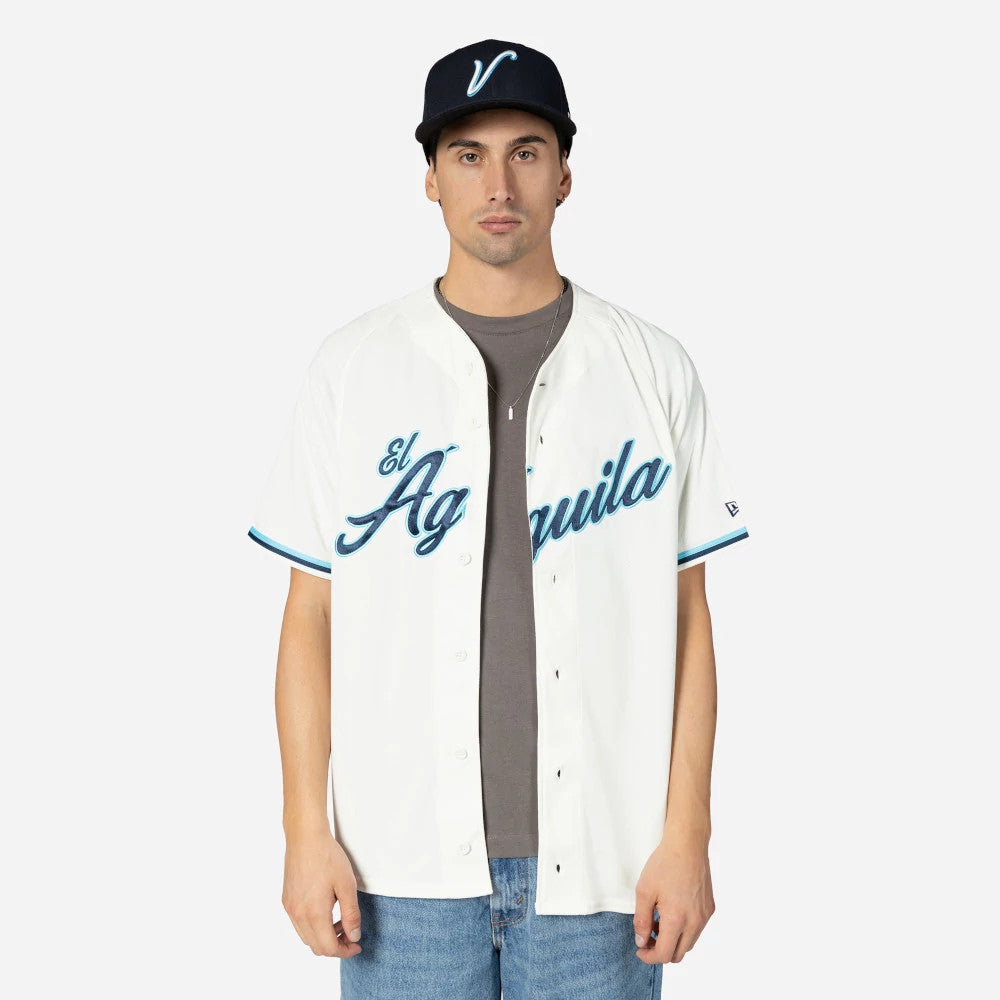 Veracruz Aguilas Mexico LMB On Field Cream On-Field Jersey, front view on a model with a navy cap, featuring blue El Aguila script across the chest, black button-up closure, and blue-tipped sleeve cuffs.