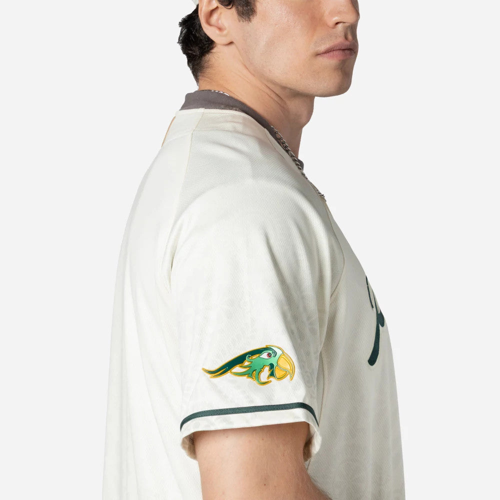 Puebla Pericos Mexico LMB On Field White On-Field Jersey, side view on a model showing the colourful parrot logo embroidered on the left sleeve above dark green piping and matching collar trim.