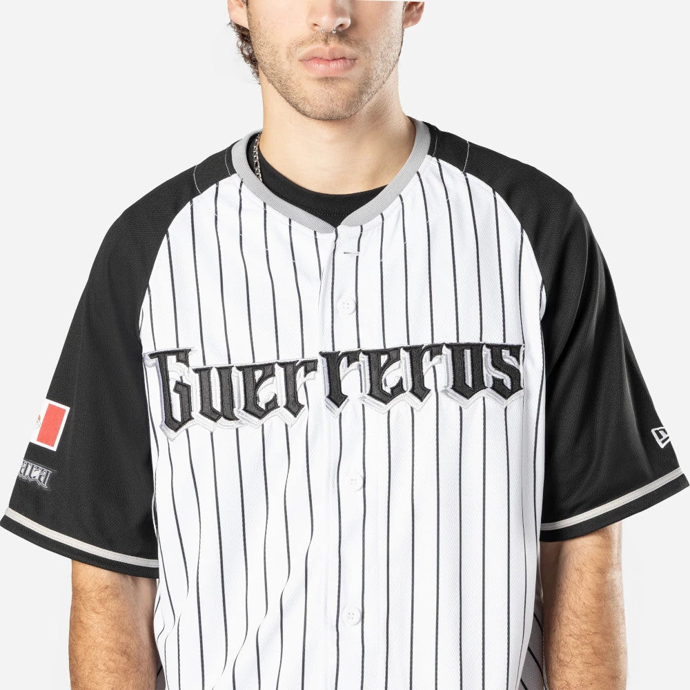 Oaxaca Guerreros Mexico LMB On Field White On-Field Jersey, front view on a model showing the black and grey Guerreros lettering across the chest, with black raglan sleeves featuring a white and red logo patch on the right sleeve.