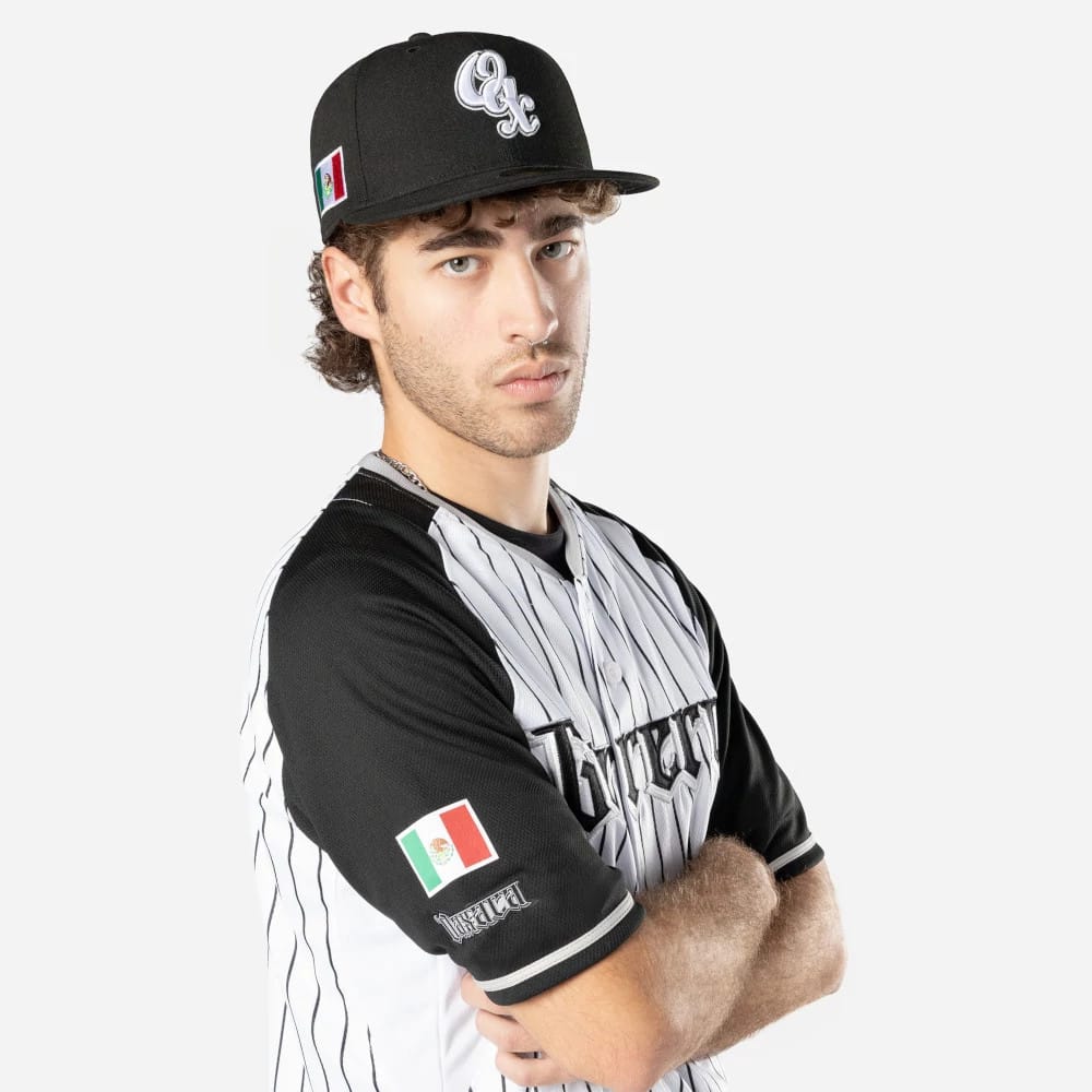 Oaxaca Guerreros Mexico LMB On Field White On-Field Jersey, on-model view with the player in a black cap featuring a white embroidered QC logo on the front panel and a Mexican flag patch on the left sleeve.