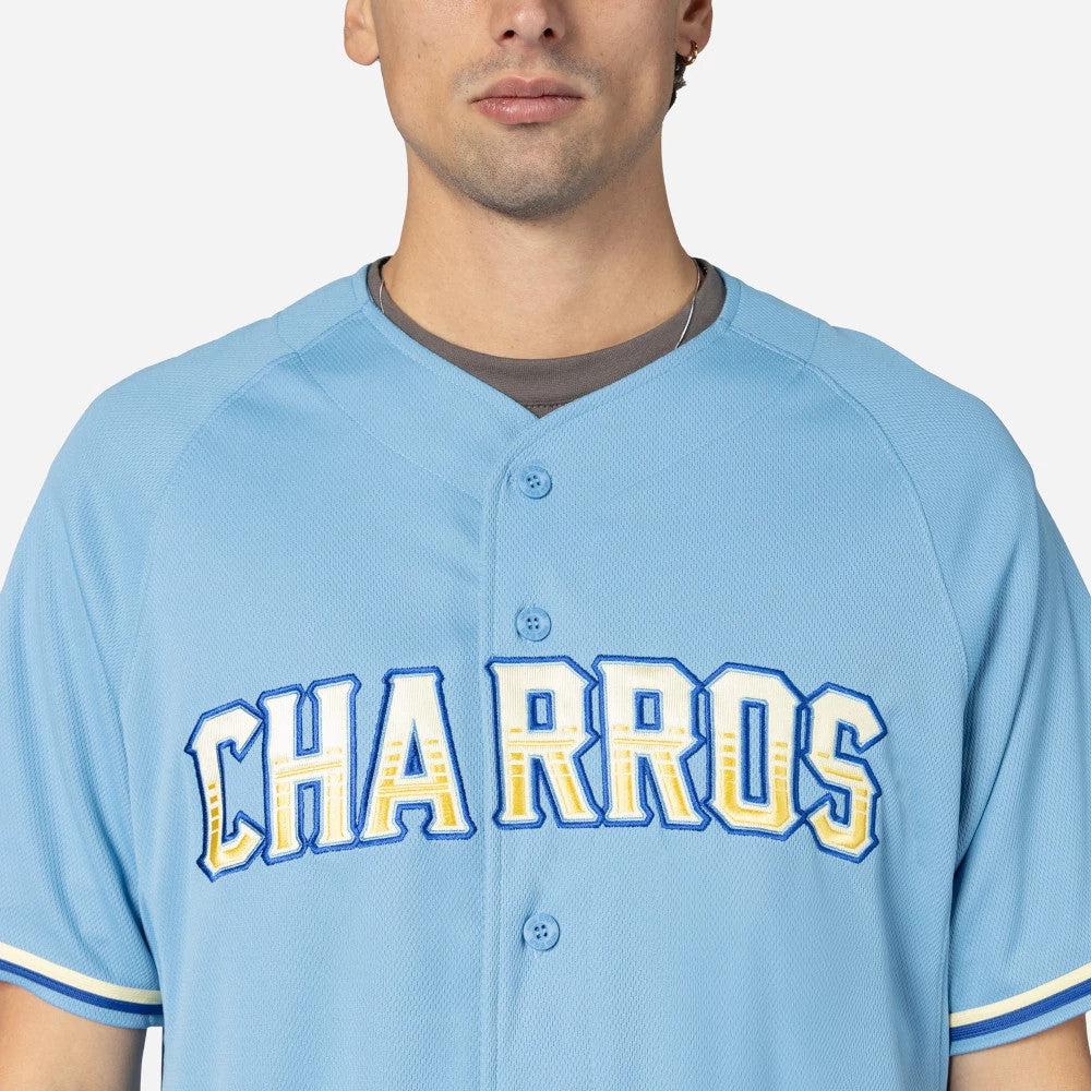 Charros De Jalisco Mexico LMB On Field Pastel Blue On-Field Jersey, front view on a model showing the bold white, yellow, and blue embroidered CHARROS lettering across the chest and matching pastel blue buttons.