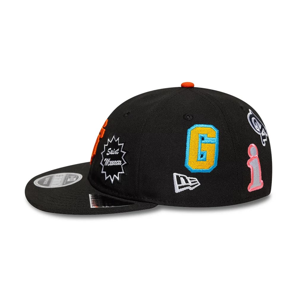 San Francisco Giants MLB X Saint Mxxxxxx Black Retro Crown New Era 9FIFTY Snapback Adjustable Cap, side view showing the New Era flag logo on the left side and colourful embroidered graphics including a large G and pink i on the black crown.