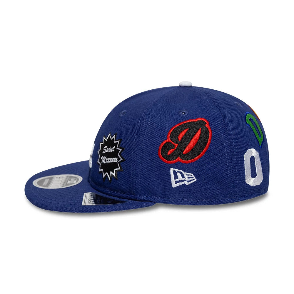 LA Dodgers MLB X Saint Mxxxxxx Dark Blue Retro Crown New Era 9FIFTY Snapback Adjustable Cap, side view showing multiple embroidered logos including a central red D logo, New Era flag logo, and a grey 9FIFTY size sticker on the visor.