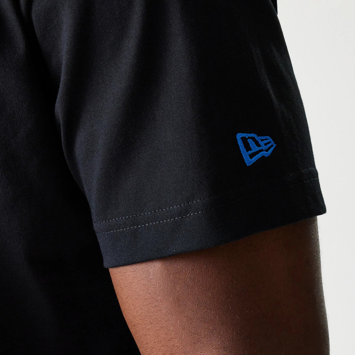 LA Dodgers MLB Paisley Black Oversized T-Shirt, side view showing the black fabric with a blue embroidered New Era logo on the sleeve edge, highlighting the simple stitching detail of the short sleeve hem.