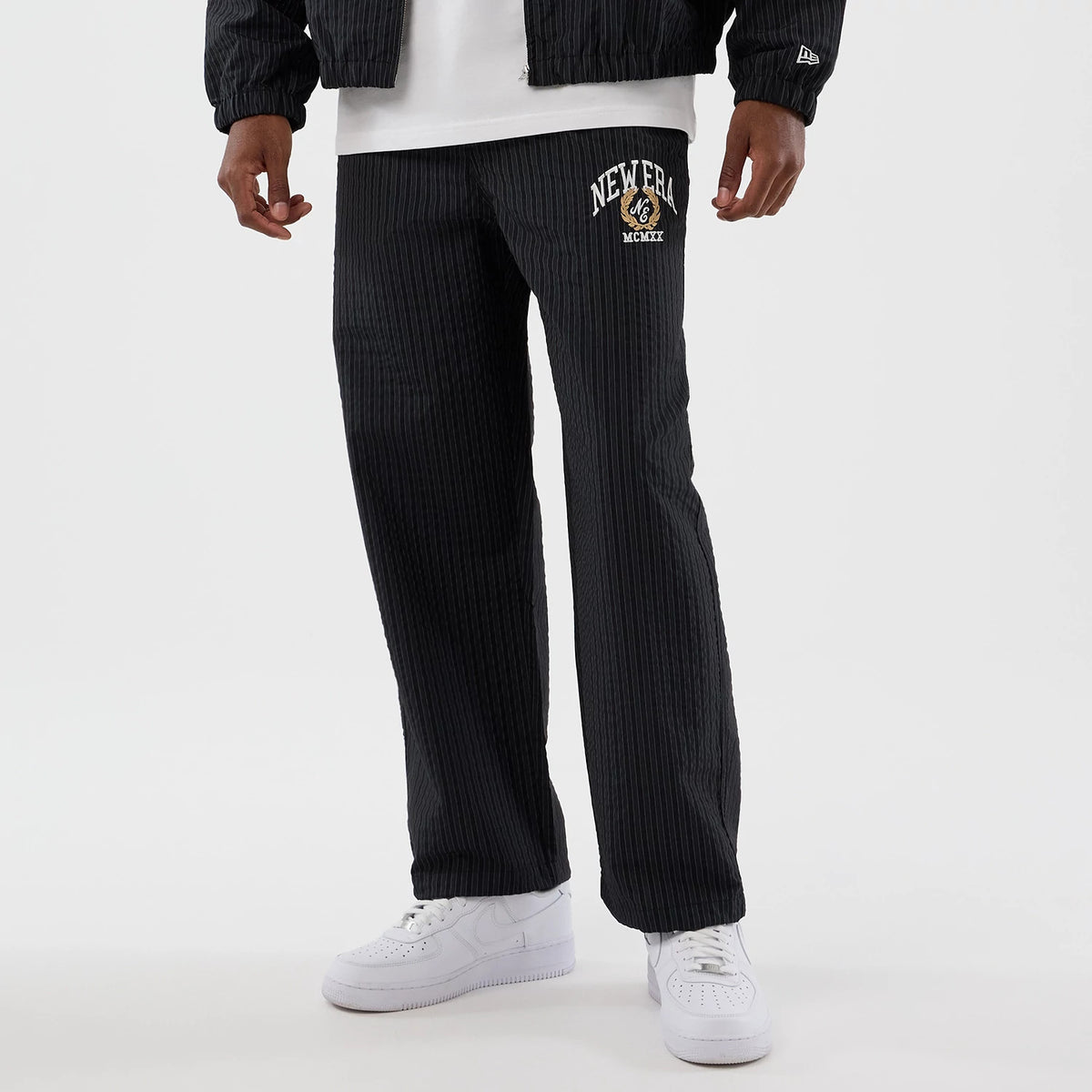 New Era Street Class Navy Straight Leg Joggers, front view on a model wearing a matching jacket and white trainers, featuring embroidered New Era MCMLXX text and logo on the left upper leg against a pinstriped navy fabric.