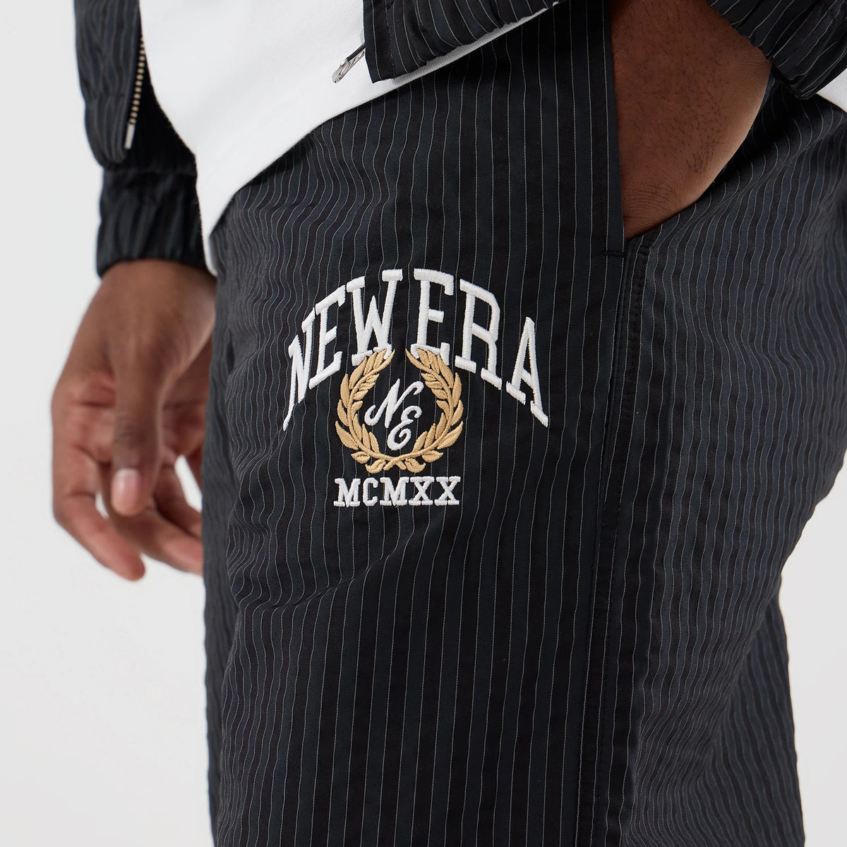 New Era Street Class Navy Straight Leg Joggers, close-up with a pinstripe design featuring white and gold embroidered NEW ERA graphics and MCMXX lettering on the upper leg, styled with a white top and matching jacket.
