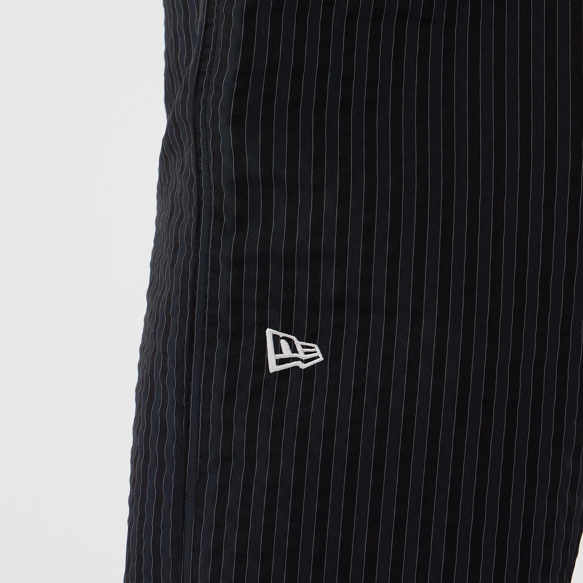 New Era Street Class Navy Straight Leg Joggers, close-up view showing thin white pinstripe detailing on the navy fabric and the white embroidered New Era flag logo positioned on the front left side.