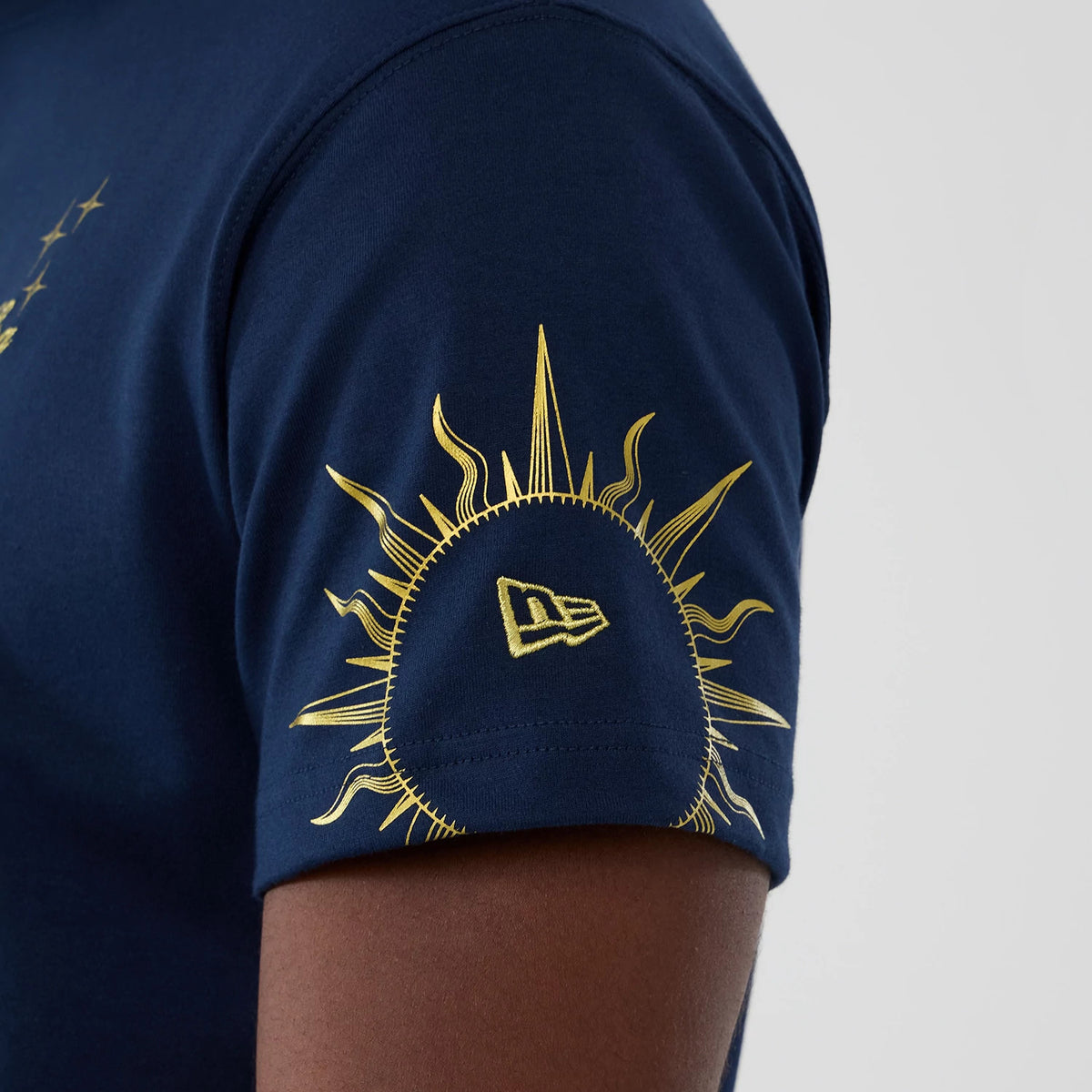 New Era Cosmic Craft Blue T-Shirt, side view showing a dark blue sleeve with a bright yellow sun graphic and a debossed New Era logo intricately placed within the sun's rays on the sleeve.