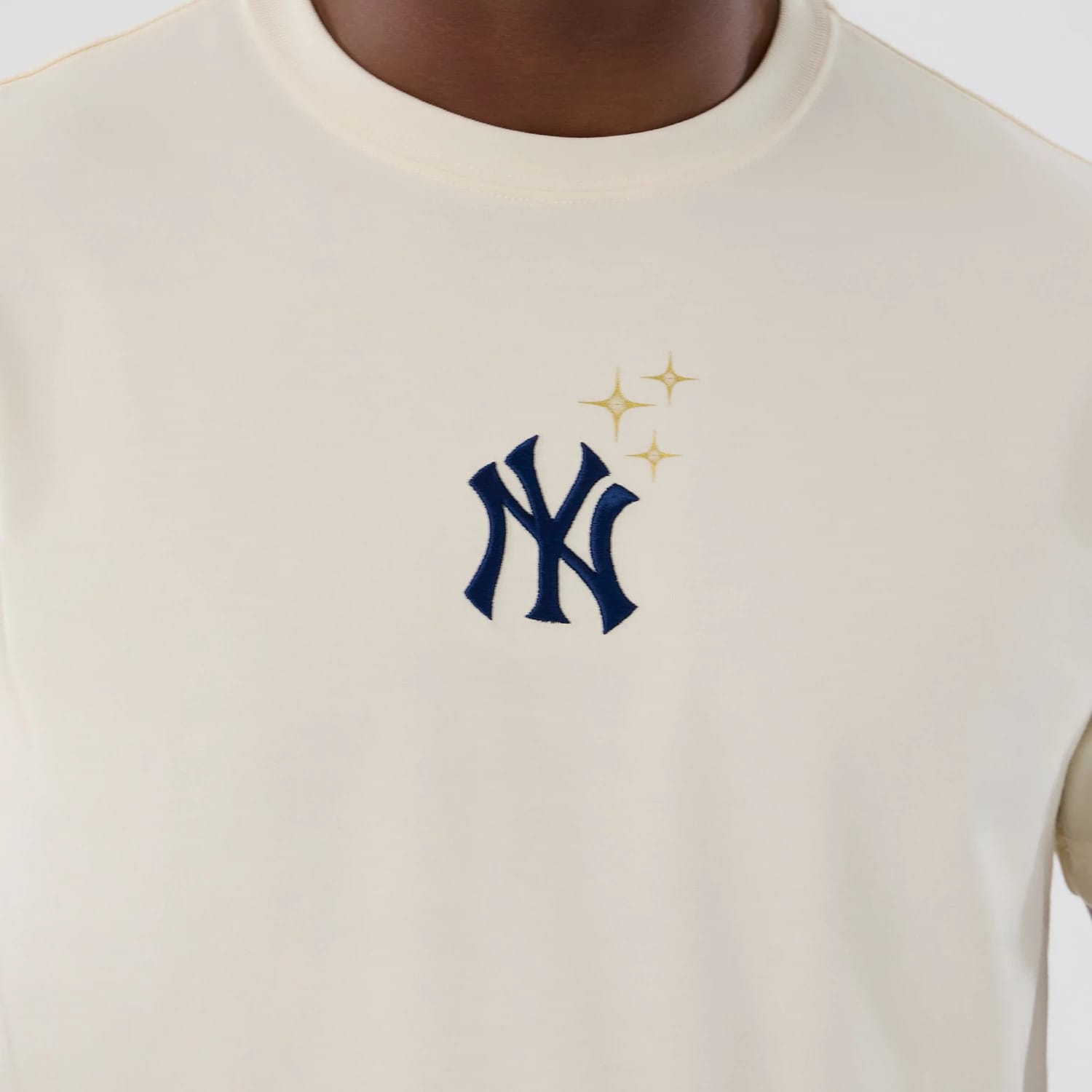 New York Yankees MLB Cosmic Craft Cream T-Shirt, front view showing a cream fabric with a navy NY Yankees logo in a raised finish on the chest, accompanied by three gold stars to the upper right of the logo.