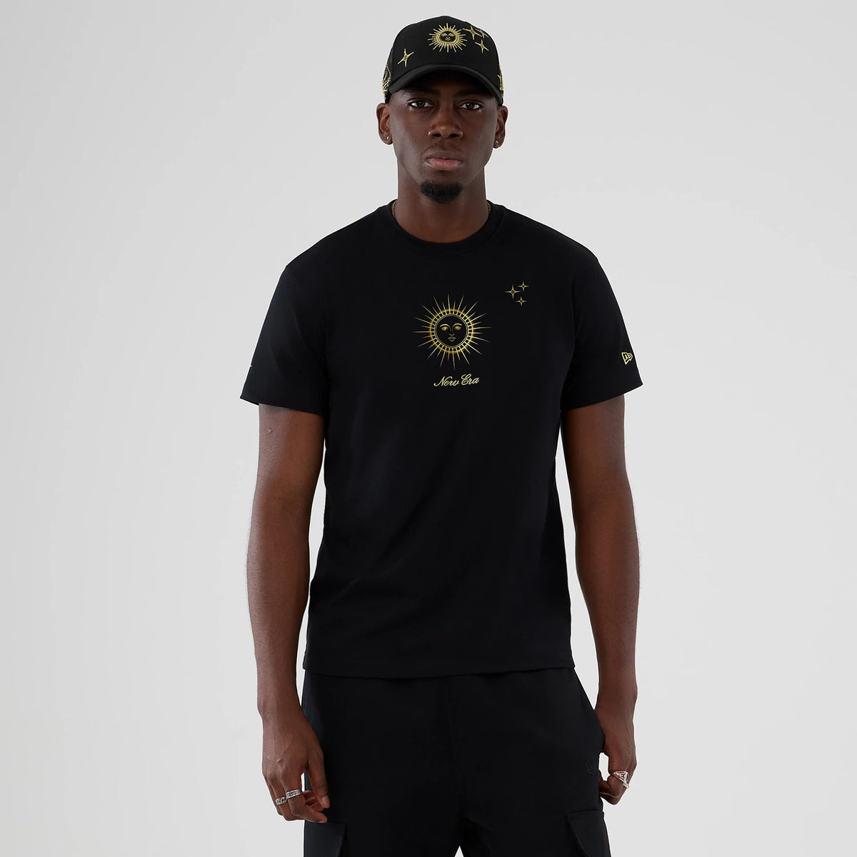 New Era Cosmic Craft Black T-Shirt, on-model view showing the black shirt with a gold sun and star design centred on the chest, New Era script beneath, and a raised New Era logo on the left sleeve.