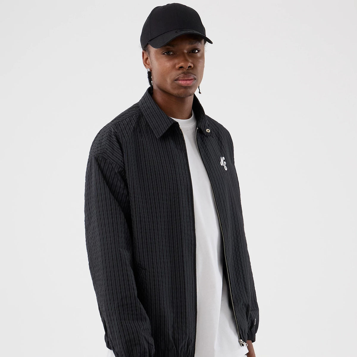 New Era Street Class Navy Jacket, on-model view showing the navy pinstriped design with white embroidered logo on the left chest, full zip closure and relaxed fit of the jacket over a white shirt and black cap.