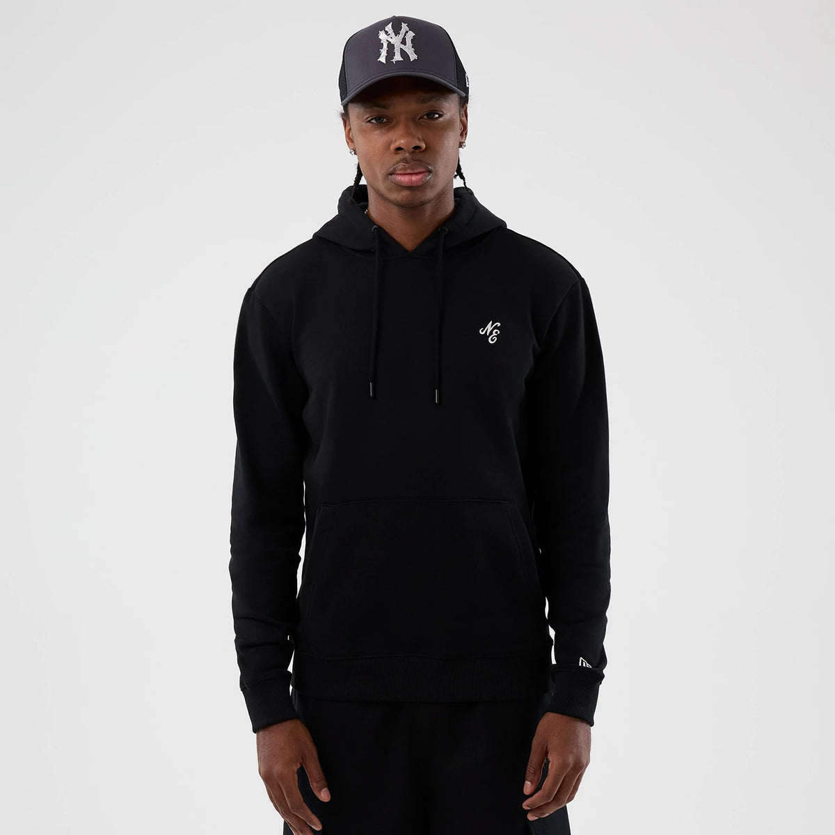 New Era Street Graphic Black Pullover Hoodie, front view showing the black hoodie worn with the NC logo embroidered on the left chest, adjustable drawstrings and a kangaroo pocket, paired with a dark cap featuring a raised NY logo.