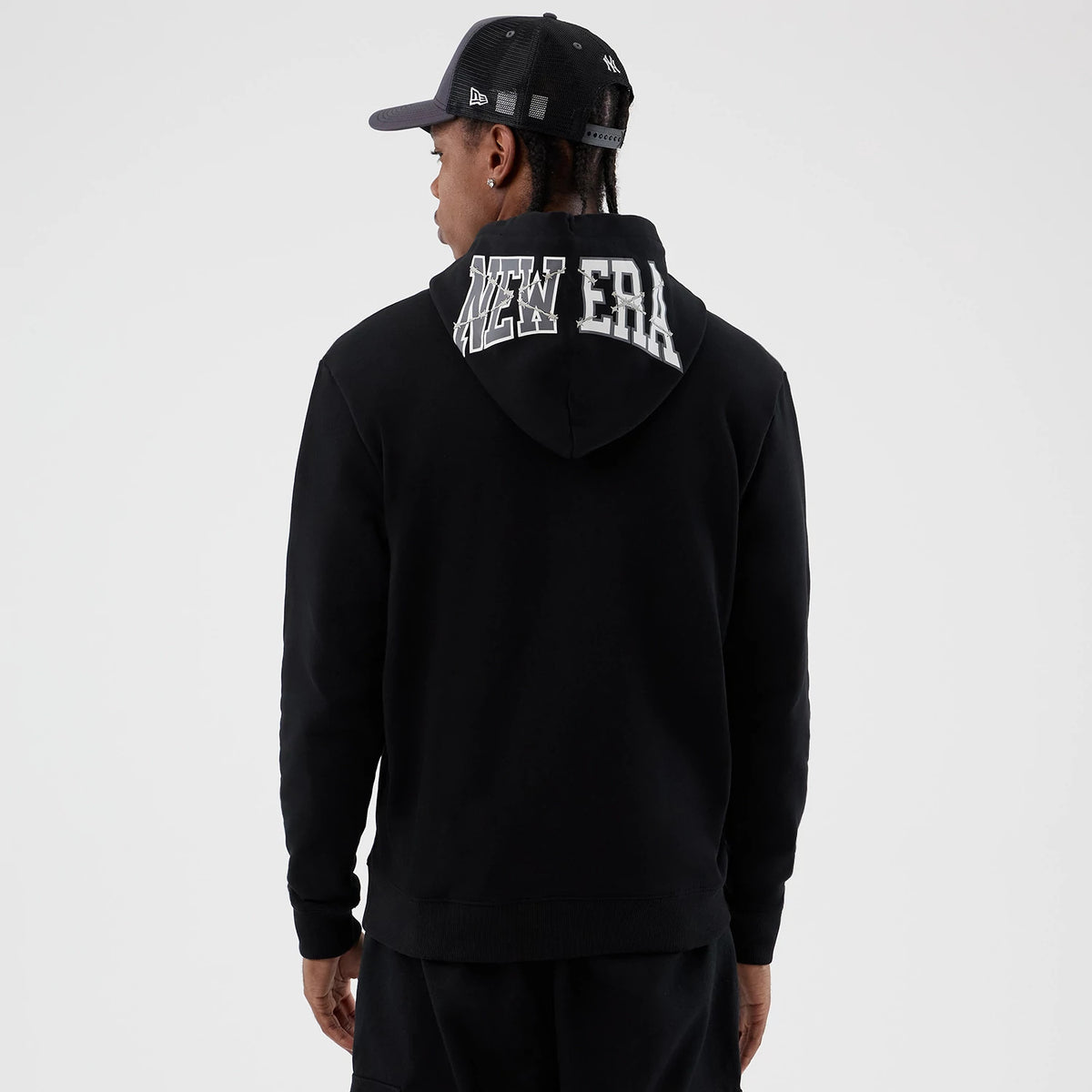 New Era Street Graphic Black Pullover Hoodie, back view featuring a large white raised New Era logo across the hood, worn by a model with a black cap showing a debossed logo on the side.