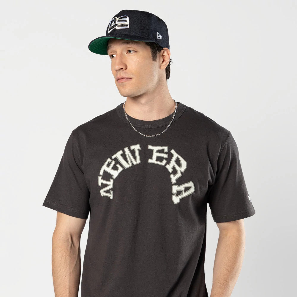 New Era Ochiai Shohei Grey T-Shirt, on-model view showing the grey shirt with "NEW ERA" printed in large white letters across the chest and a small white embroidered New Era logo on the left sleeve.