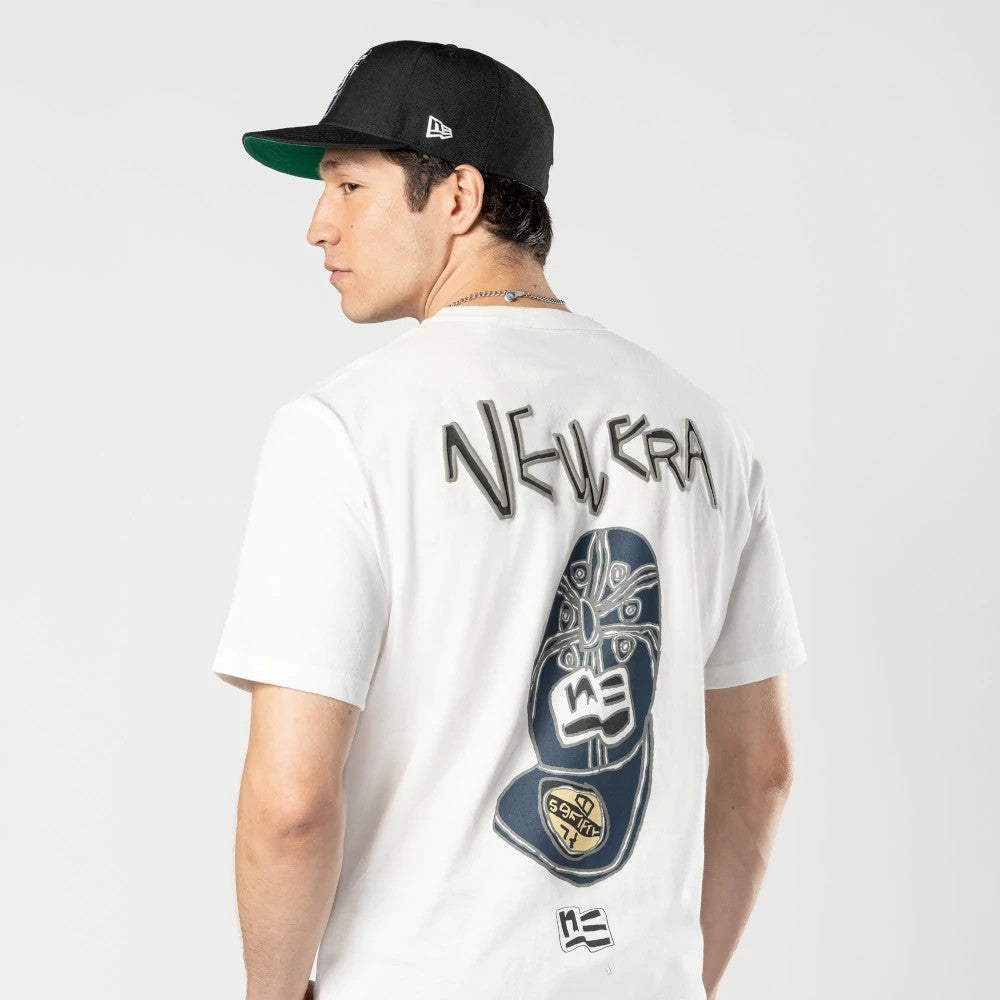 New Era Ochiai Shohei Office Cream T-Shirt, on-model view showing the back with abstract graphics featuring debossed New Era text at the top, intricate patterns in dark tones below, and a small logo near the bottom edge.