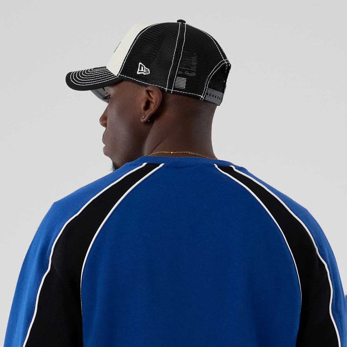 New Era Colour Block Navy Crew Neck Sweater, rear view on a model with contrasting black and white panelling and white piping detail on the sleeves, paired with a black and white mesh cap featuring the New Era flag logo on the left side.