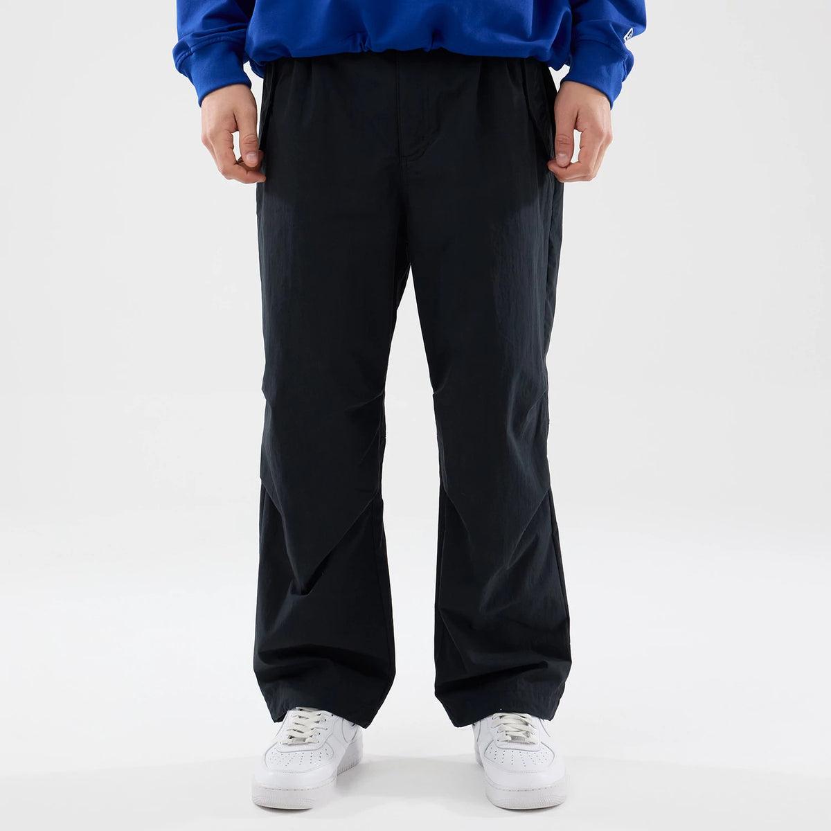 New Era Organic Black Parachute Trousers, style on a model in a relaxed fit with a blue top, showing the slightly crinkled texture and wide leg cut, paired with white trainers for a casual look.