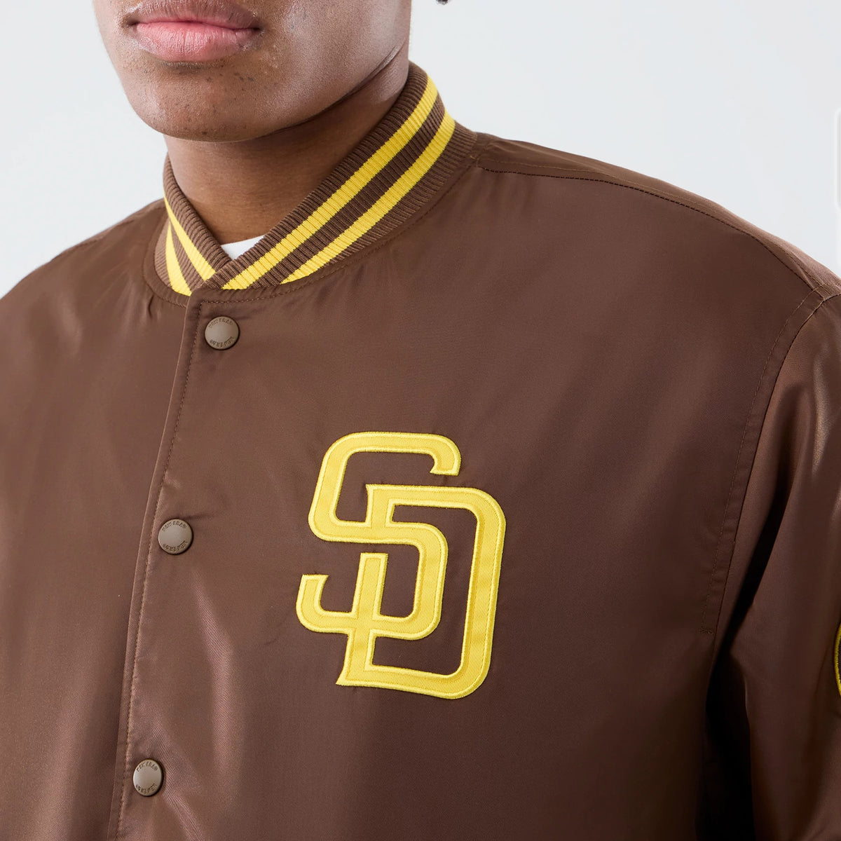 San Diego Padres MLB Authentic Dark Brown Stadium Jacket, front view showing the brown body with a raised yellow "SD" logo on the left chest, yellow and brown striped ribbed collar, and brown snap buttons along the opening.