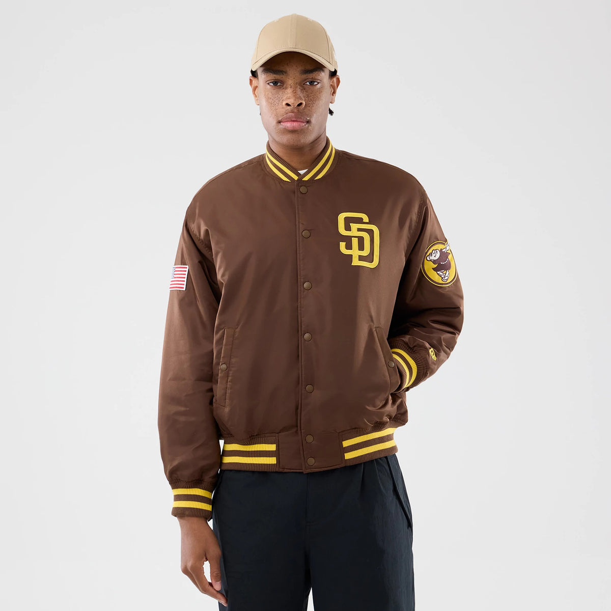 San Diego Padres MLB Authentic Dark Brown Stadium Jacket, on-model front view showing the dark brown jacket with yellow SD logo on the chest, an American flag patch on the sleeve, and yellow striped cuffs and collar.