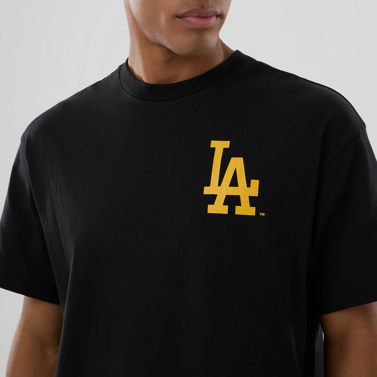 LA Dodgers MLB Neon Light Black T-Shirt, front view showing a bold yellow LA logo printed on the left chest of the plain black short-sleeved T-shirt, with a close-up of the round neckline.