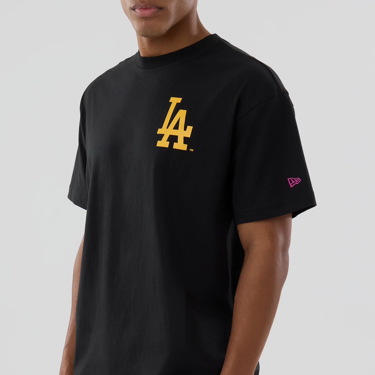 LA Dodgers MLB Neon Light Black T-Shirt, front view featuring a yellow LA logo prominently positioned on the chest and a small pink New Era logo embroidered on the sleeve, all set against a plain black background.