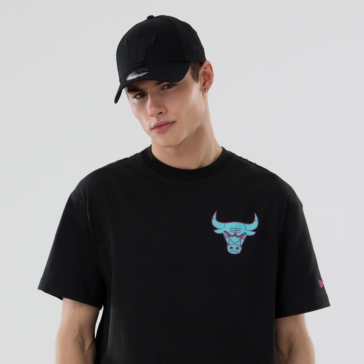 Chicago Bulls NBA Neon Light Black T-Shirt, on-model view showing the black T-shirt with a neon blue and pink Chicago Bulls logo on the chest, paired with a black cap featuring a raised logo on the front.