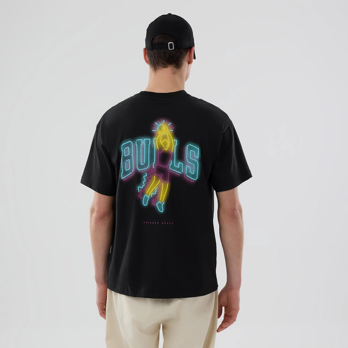 Chicago Bulls NBA Neon Light Black T-Shirt, on-model rear view showing a neon design of a basketball player in yellow and purple with the word "BULLS" in blue and neon lights effect across the back, on a black base.