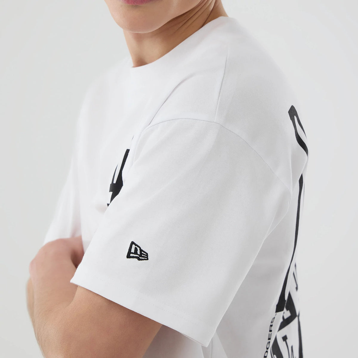 LA Dodgers MLB White T-Shirt, side view showing the clean white fabric with a black New Era logo embroidered on the sleeve and partial black graphic design extending from the back to the side.