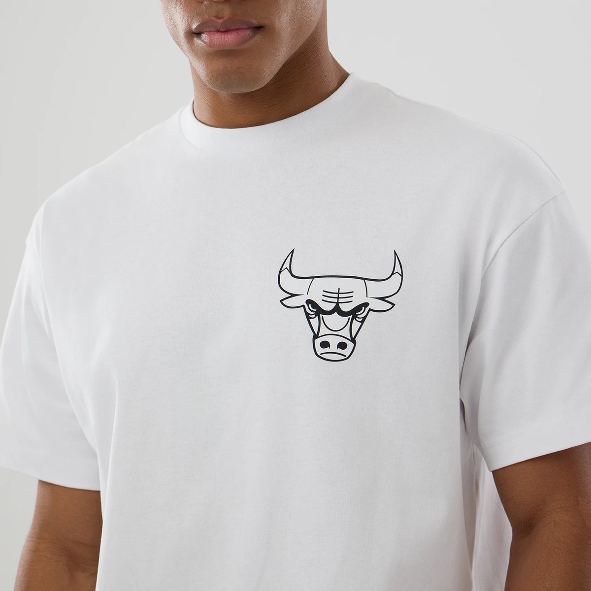 New Era Chicago Bulls NBA World White T-Shirt, front view showing a white tee with a black outlined Bulls logo on the left chest, worn by a model with short sleeves and a round neckline.
