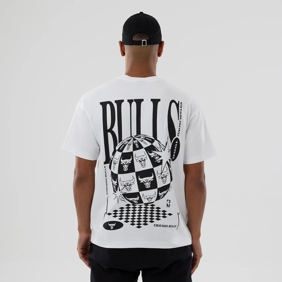 Chicago Bulls NBA World White T-Shirt, rear view showing bold black graphic design featuring oversized "BULLS" text, checkerboard globe with team logos and stars, and "CHICAGO BULLS" text near the hem on a white shirt.