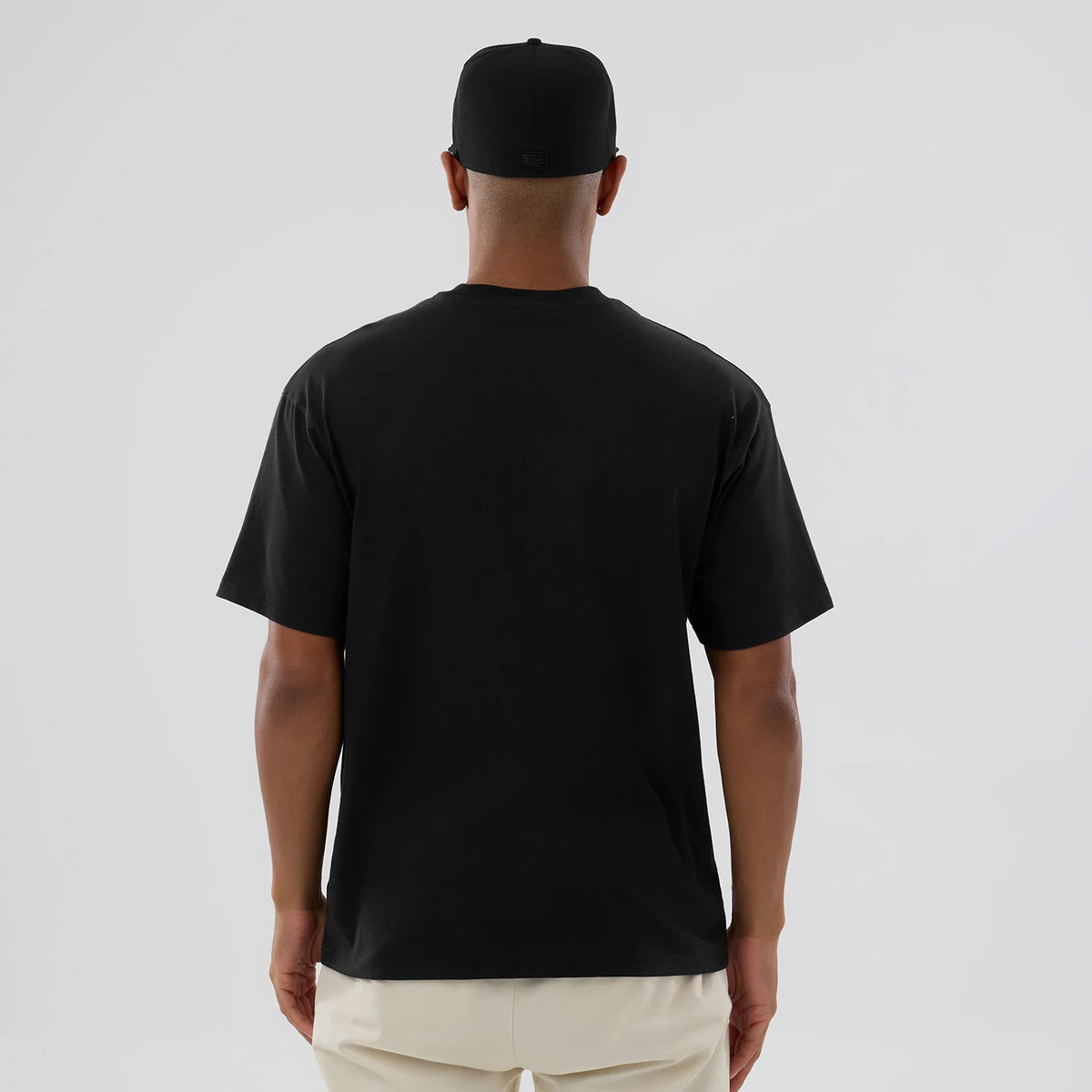 LA Dodgers MLB On Fire Black Oversized T-Shirt, rear view showing a plain black T-shirt with short sleeves and a relaxed fit, worn by a person with a black cap featuring a debossed logo centred at the back.