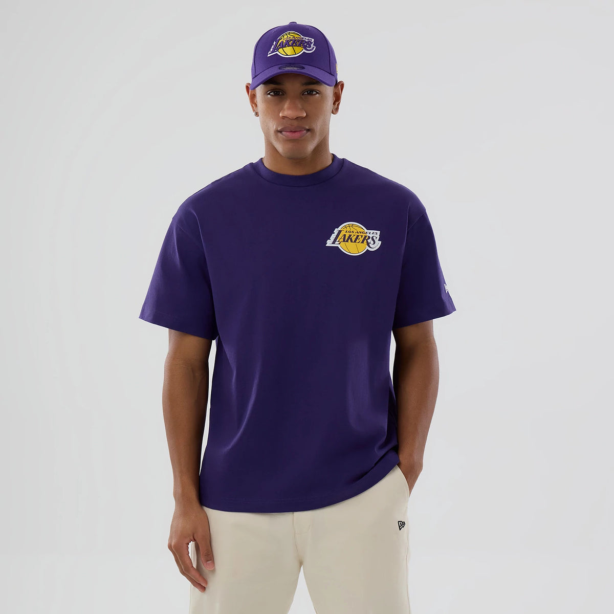 LA Lakers NBA logo Purple T-Shirt, on-model front view showing the purple T-shirt with a large LA Lakers logo printed on the left chest, paired with a matching purple cap featuring an identical logo on the front.