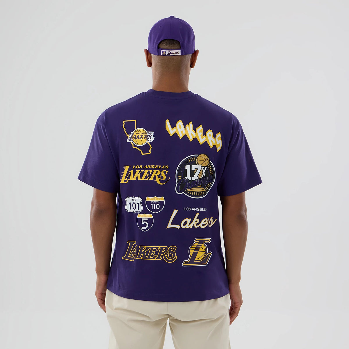 LA Lakers NBA logo Purple T-Shirt, rear view showing a series of Lakers-themed graphics including the team name, a map outline, and a 17X Champions emblem, with a man wearing a matching purple cap.