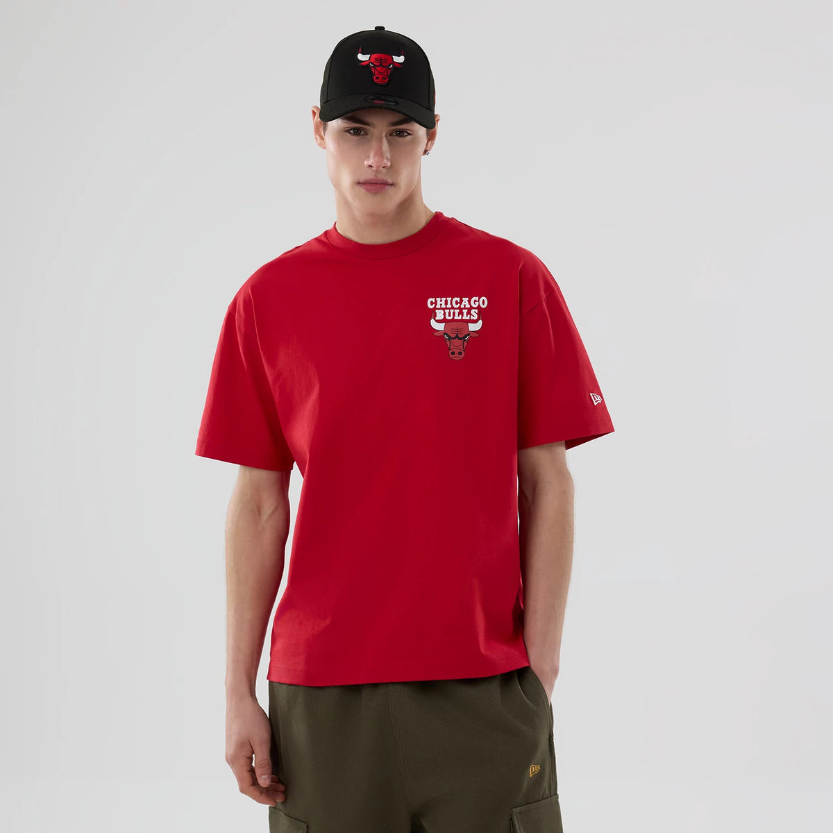Chicago Bulls NBA logo Red T-Shirt, on-model view showing the vibrant red fabric with a raised Chicago Bulls logo on the chest, a small iconic New Era logo embroidered on the left sleeve, and paired with a black cap featuring the Bulls logo.