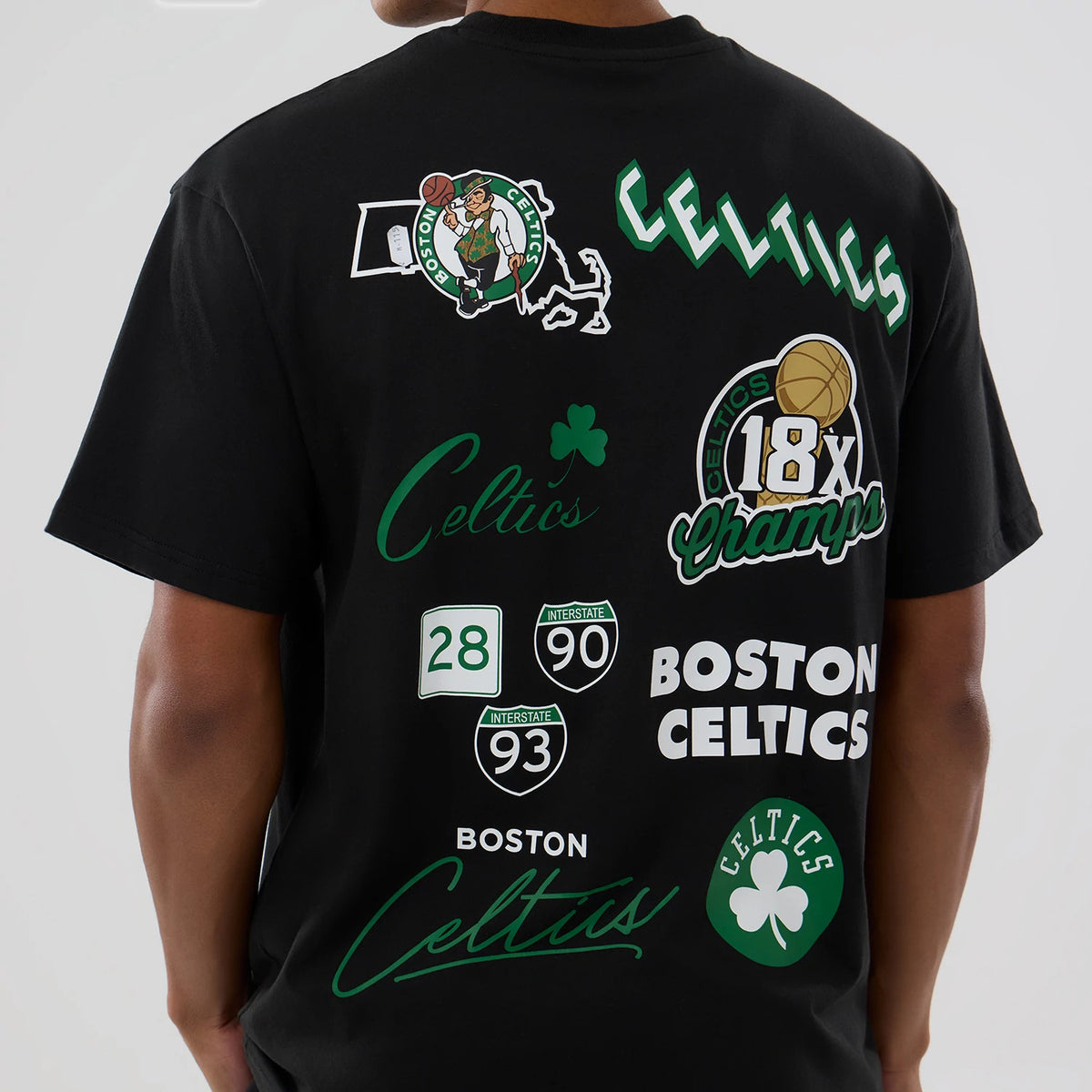 Boston Celtics NBA logo Black T-Shirt, rear view showing multiple green and white graphics including the Celtics logo, text "Celtics" and "Boston Celtics," and designs resembling road signs, all spread across the back of the black fabric.
