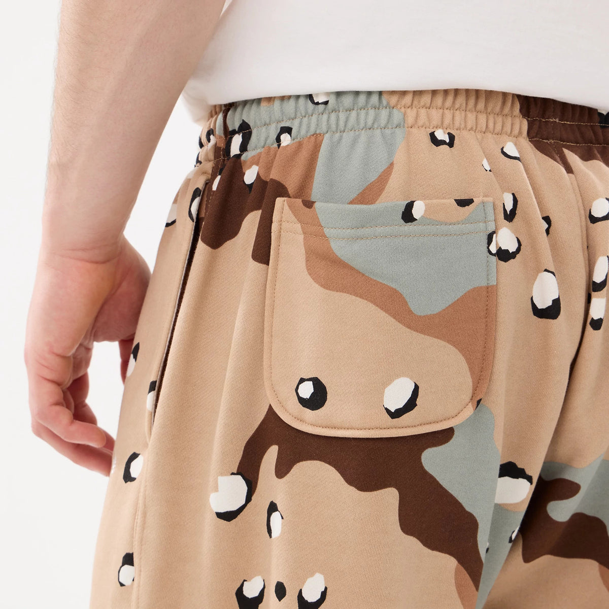 New Era Desert Camo Joggers, side view with a close-up of the desert camo pattern, showing the elastic waistband, side pocket detail, and model wearing a white T-shirt for a casual look.